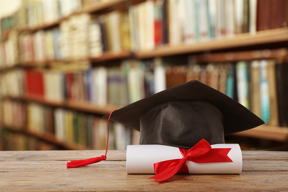 Diploma,And,Graduation,Hat,On,Wooden,Table,In,Library Diploma e cappello graduato su tavolo in legno in biblioteca