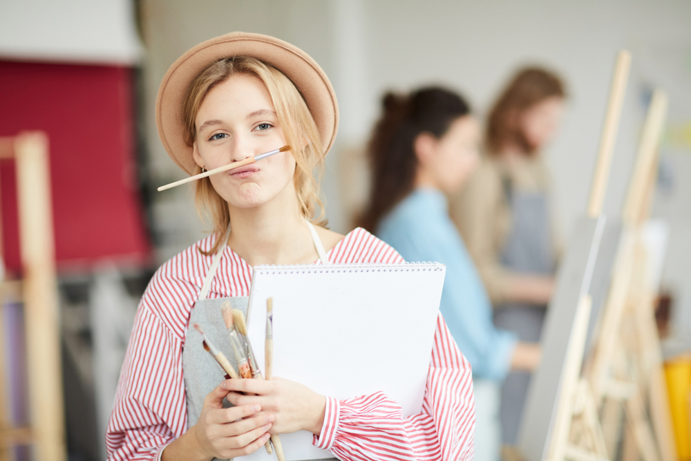studentessa di belle arti arriccia la bocca e fa una smorfia col pennello